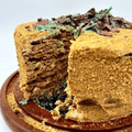 A Peppermint Crisp Tart Cake with layers of chocolate and whipped cream, garnished with crushed peppermint candies on top, served on a wooden plate.